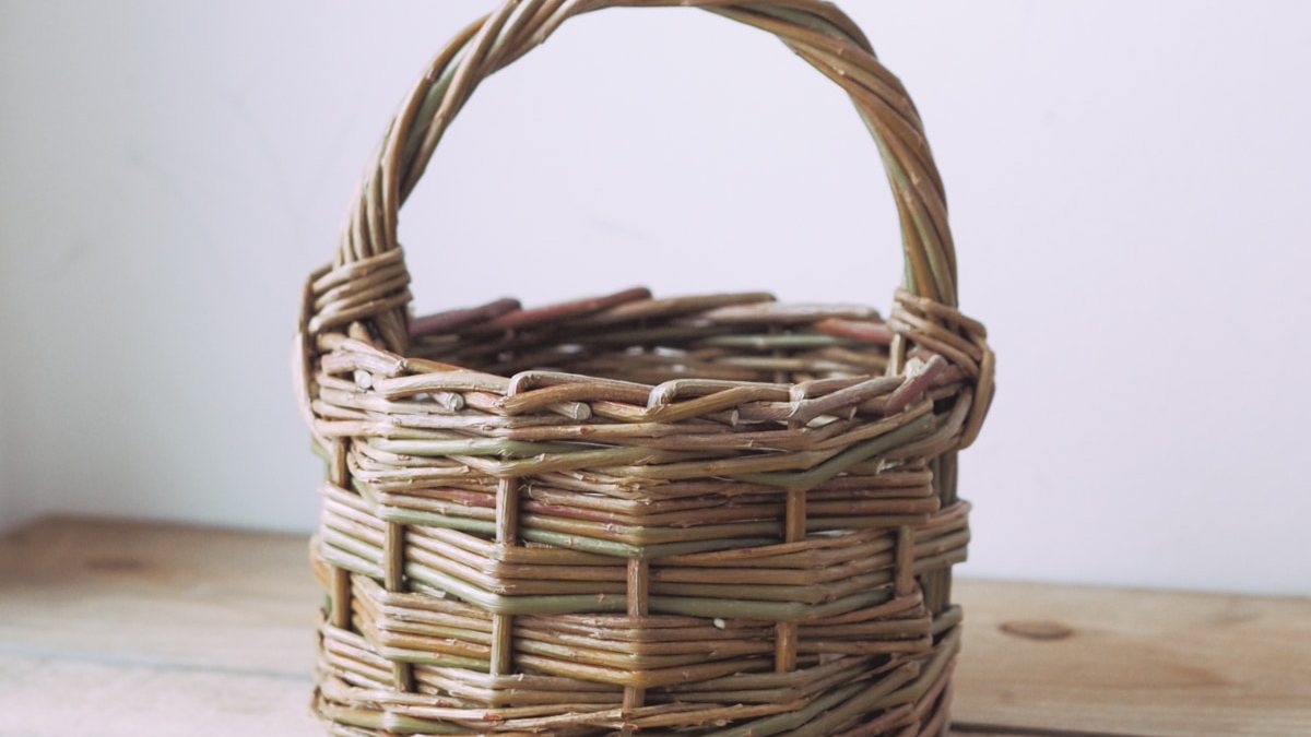 A round willow berry basket with an arched handle, standing on a wooden table.