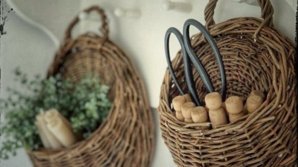 Two woven willow wall baskets hanging on a pale wall, one holding trailing greenery.