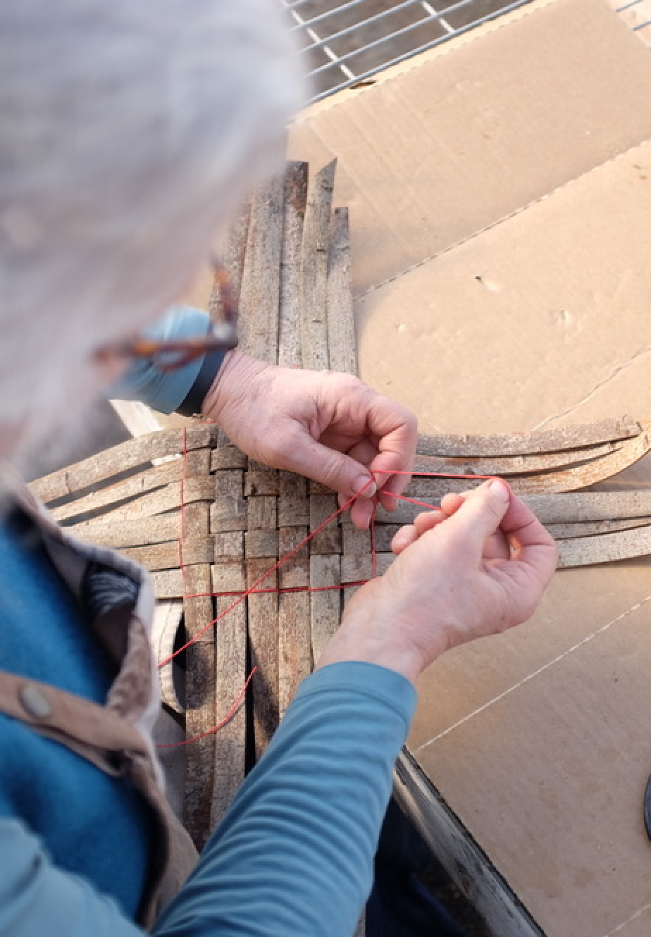Close-up of hands weaving a willow basket.