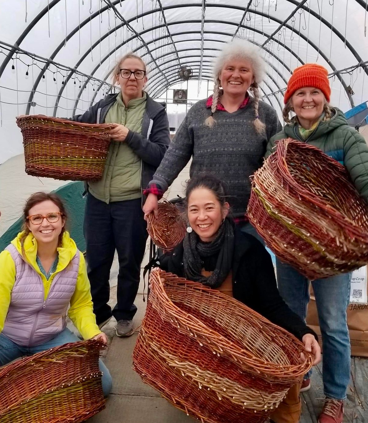 Five guild members standing together inside a greenhouse, each holding a large woven willow basket.