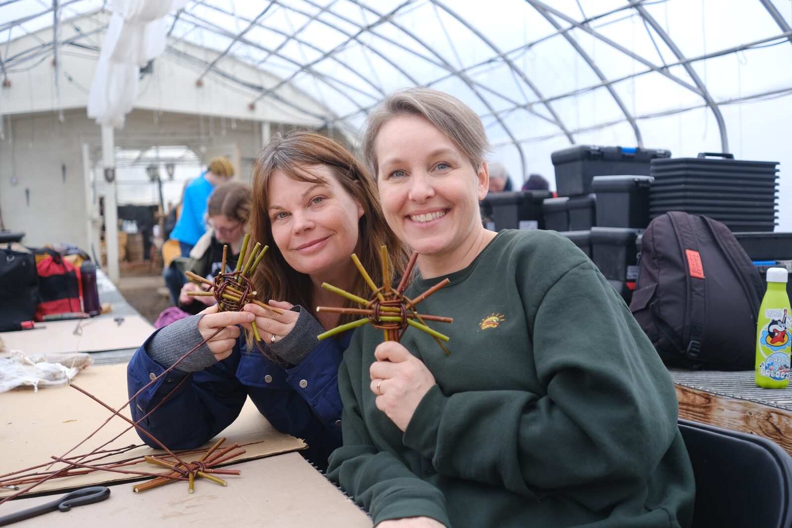 Two weavers in a greenhouse holding up the woven willow stars they have just made.