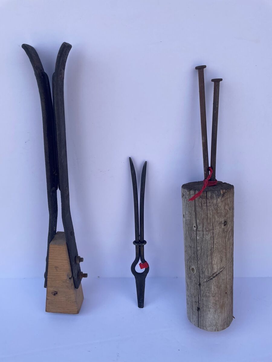Three willow-stripping tools side by side: two forked steel tools from England and a homemade one made from two nails set in a block of wood.