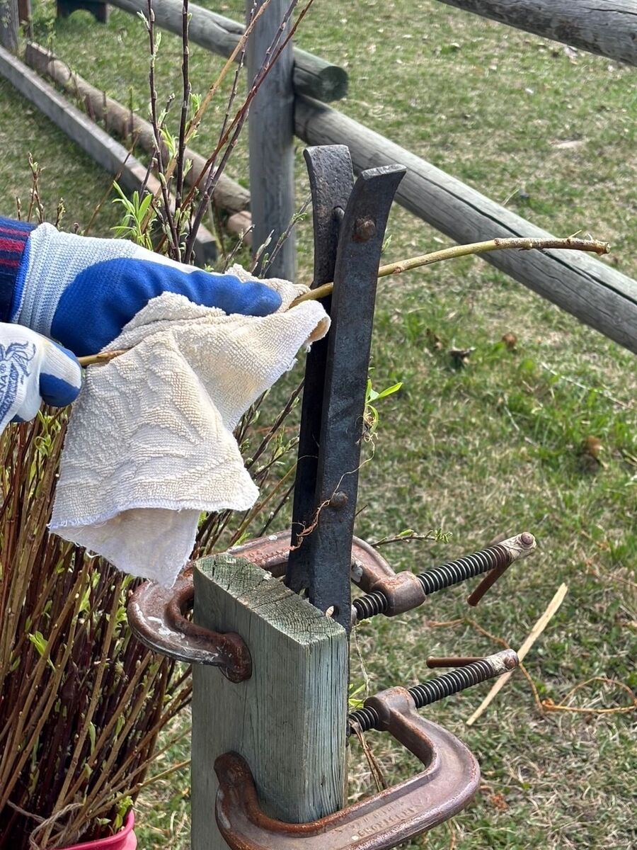 A gloved hand steadying a rod with a cloth while pulling it through a second, differently shaped tool.